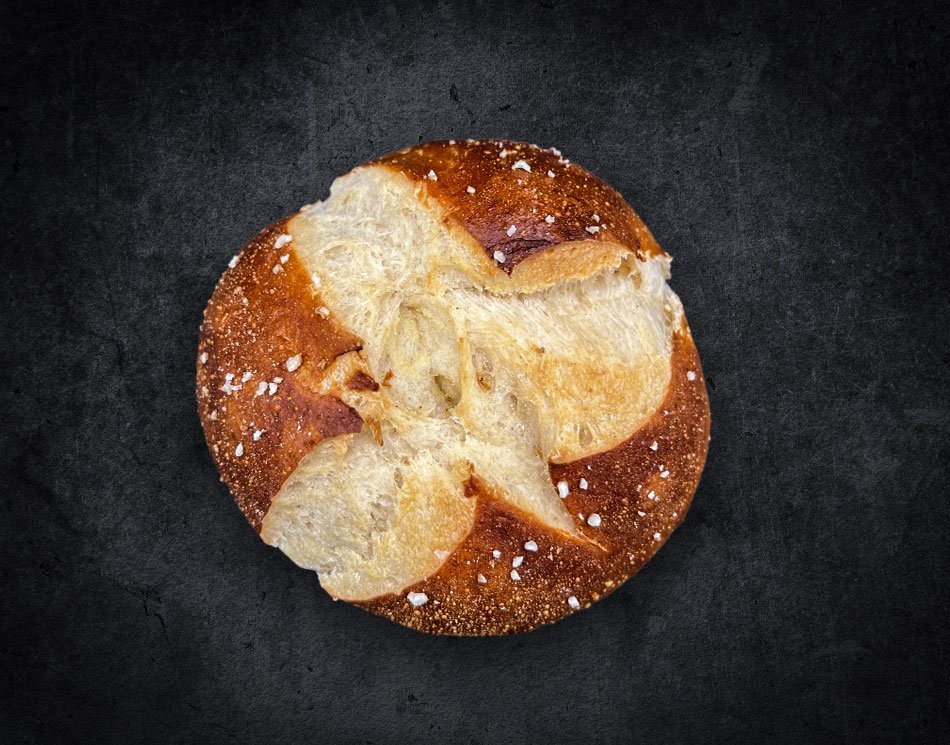 Ein Laugen-Brötchen mit groben Salz-Körnern. Es ist goldbraun und rund.